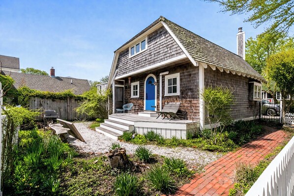A two-story house with a front porch, steps leading to the entrance, and a small garden area.