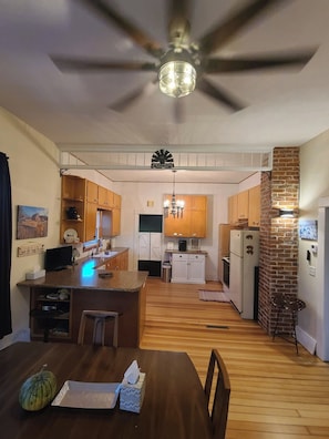 Una cocina con armarios de madera, una isla central, un ventilador de techo y una pared decorativa de ladrillo.