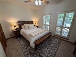A bedroom with a bed, bedside lamps, a clock, a ceiling fan, and windows with blinds.