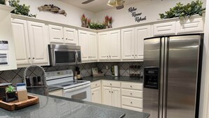 A kitchen with white cabinets, stainless steel appliances, a granite countertop, and decorative plants. - The Bass Shack (Alba)