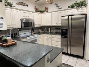 A kitchen with white cabinets, stainless steel appliances, a granite countertop, and decorative plants.