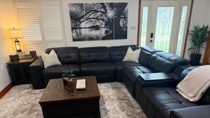 A living room with a sectional sofa, a coffee table, a lamp, and a large black and white artwork on the wall. - The Bass Shack (Alba)
