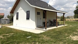 A small white house with a porch and a covered patio area. - Country Cottage - New Construction On 20 acres (Miles City)