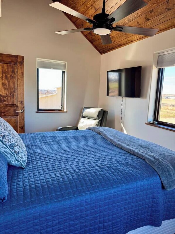 A bedroom with a bed, a ceiling fan, a TV, and a window.