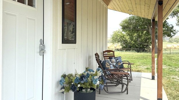 A covered porch with a wooden ceiling, a white door, and a potted plant. - Country Cottage - New Construction On 20 acres (Miles City)