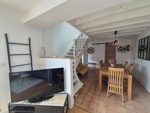 A living room with a TV, a staircase, a dining area with chairs and a table, and a wall with decorative items.