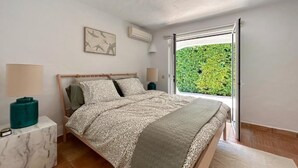 A bedroom with a bed, a nightstand, a lamp, and a view of greenery through a sliding door. - Casa di Campara Villa Faro (Faro)
