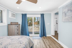 Camera da letto con un letto, una ventola a soffitto, una porta scorrevole in vetro su un patio e un comò in legno.