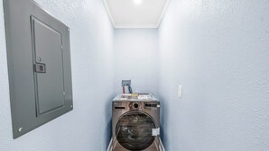 A laundry room with a washing machine, a door, and a light switch on the wall. - Serene 1-bedroom  in St. Pete Beach - UNIT B (St. Pete Beach)