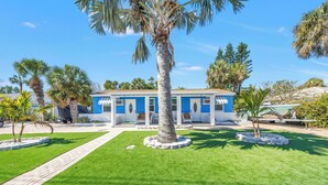 A blue building with a white porch, surrounded by well-maintained grass and palm trees. - Serene 1-bedroom  in St. Pete Beach - UNIT B (St. Pete Beach)