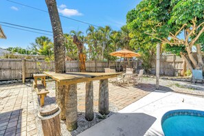 Un giardino con tavolo e sedie in legno, una piscina e palme.