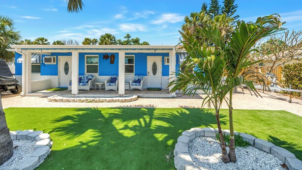 A blue building with a covered patio, a palm tree, and a well-maintained lawn. - Serene 1-bedroom  in St. Pete Beach - UNIT B (St. Pete Beach)