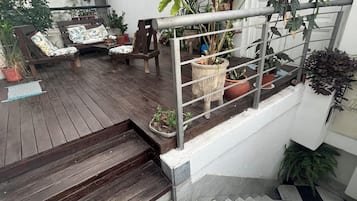 Una terraza de madera con mobiliario exterior, plantas en macetas y una escalera que lleva a un nivel superior.
