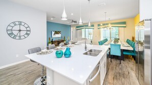 A modern kitchen with a central island, pendant lighting, and a clock on the wall. - Upstay Sleeps 26 w Private Pool, Hot Tub, Games (Kissimmee)