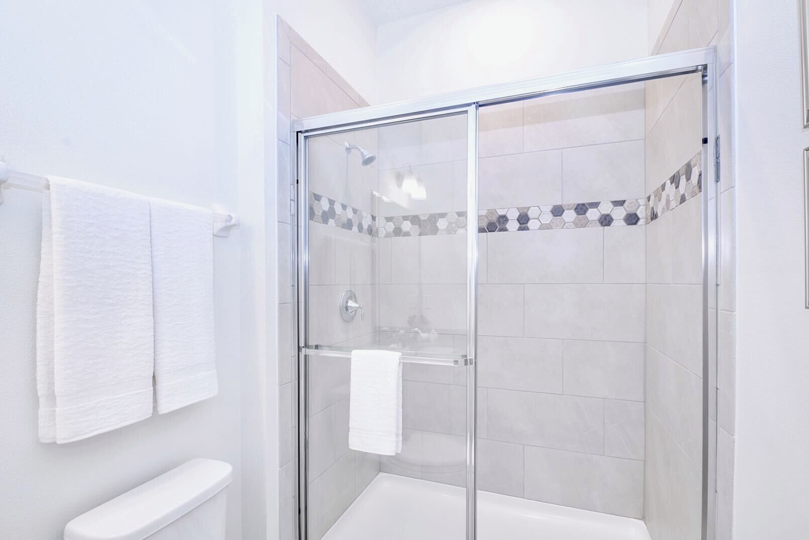 A modern bathroom with a glass-enclosed shower, white tiles, and a visible towel rack.