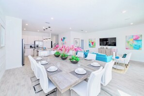 Una cocina moderna con armarios blancos, horno empotrado y comedor con mesa de madera dispuesta para seis.