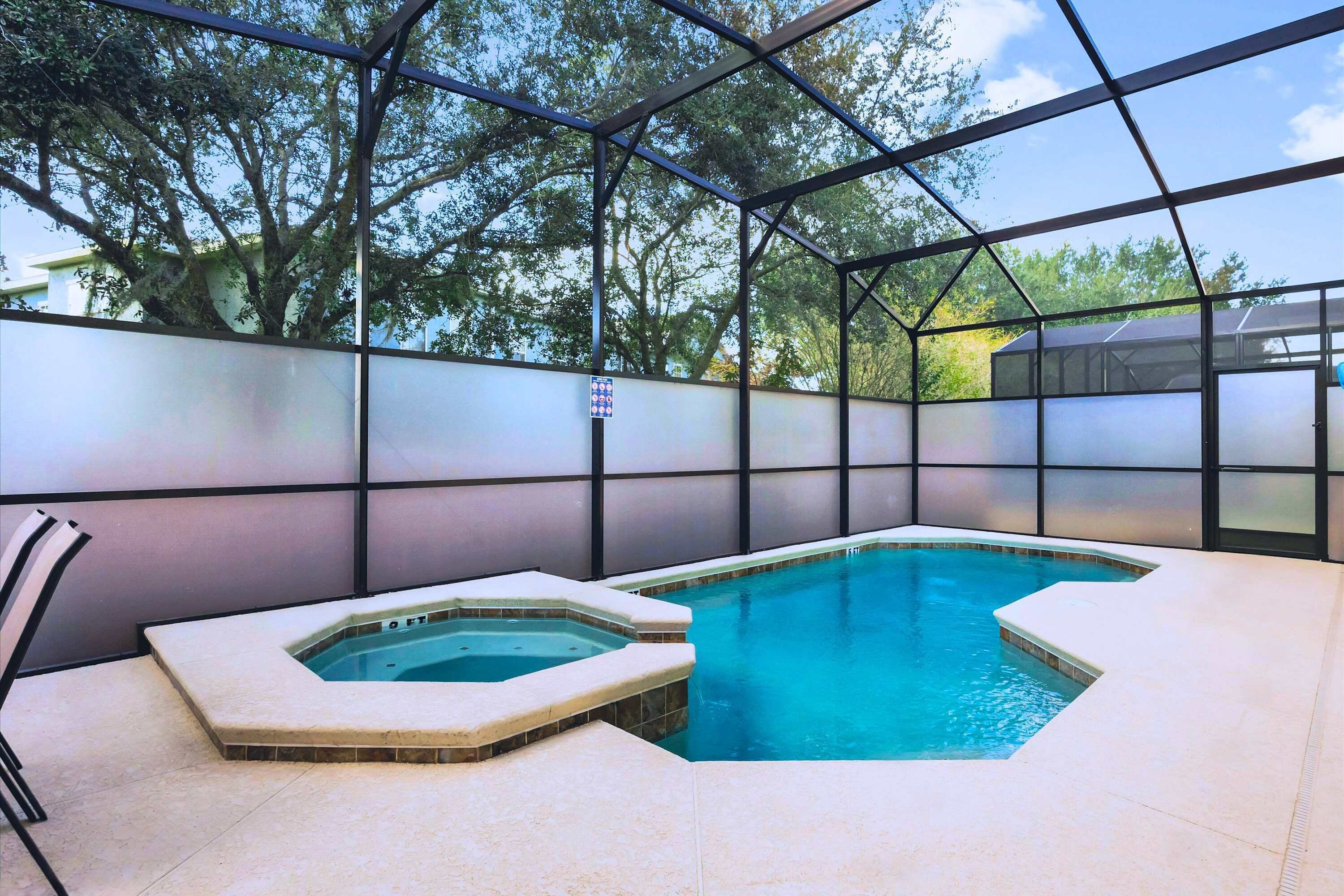 Una piscina con cerramiento de vidrio, rodeada por una estructura metálica y suelo de baldosas.