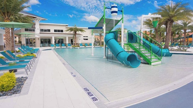 Zona de piscina con tobogán de agua, sillas de descanso y un edificio al fondo.