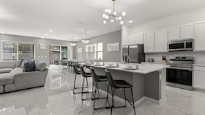 A modern kitchen with white cabinets, stainless steel appliances, and a central island with bar stools. - Upstay Resort Villa - Pool, Hot Tub, Sleeps 27 (Kissimmee)
