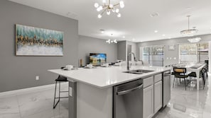 A modern kitchen with a large island, stainless steel appliances, and a dining area with a view. - Upstay Resort Villa - Pool, Hot Tub, Sleeps 27 (Kissimmee)