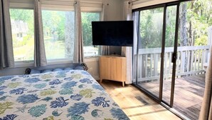 Makuuhuoneessa on sänky, televisio, lasiliukuovi ja näkymä puita kohti.