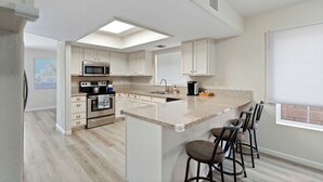 Una cucina moderna con isola centrale, sgabelli da bar, microonde, forno e una finestra con persiane.