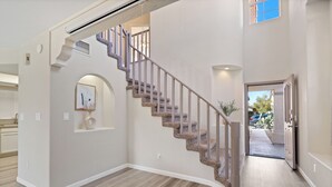 Un interno moderno con una scala a forma di arco, un corridoio che conduce a una porta e una piccola pianta.