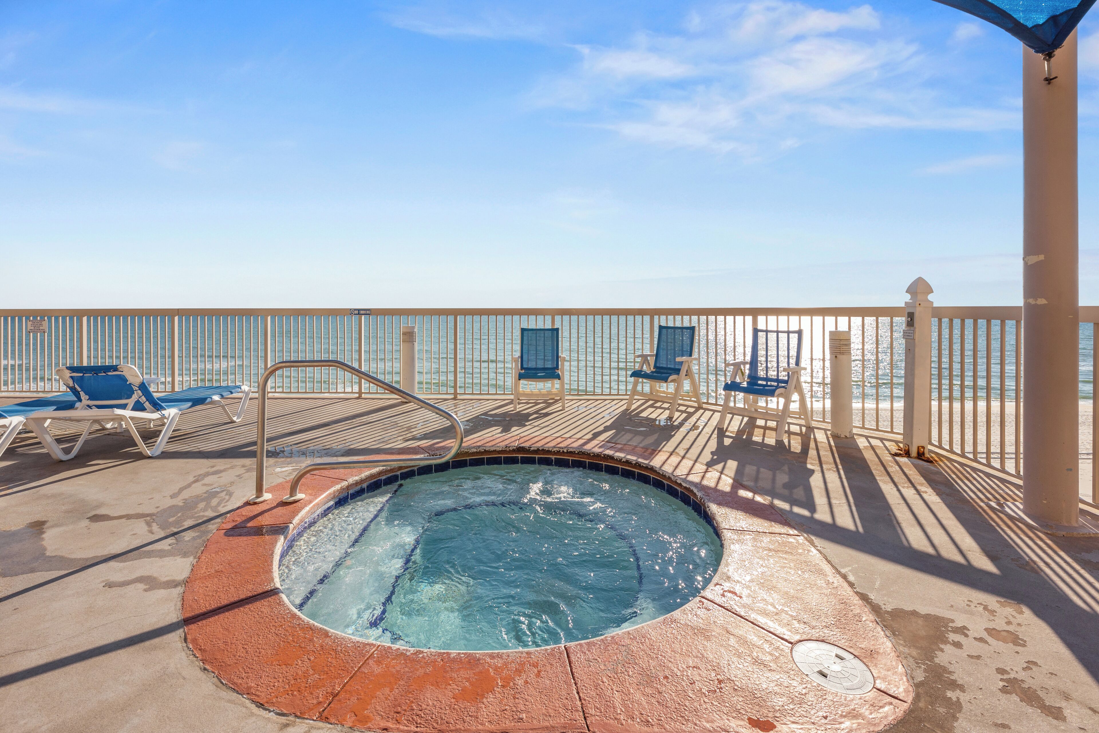 A pool area with a hot tub, lounge chairs, and a view of the ocean.