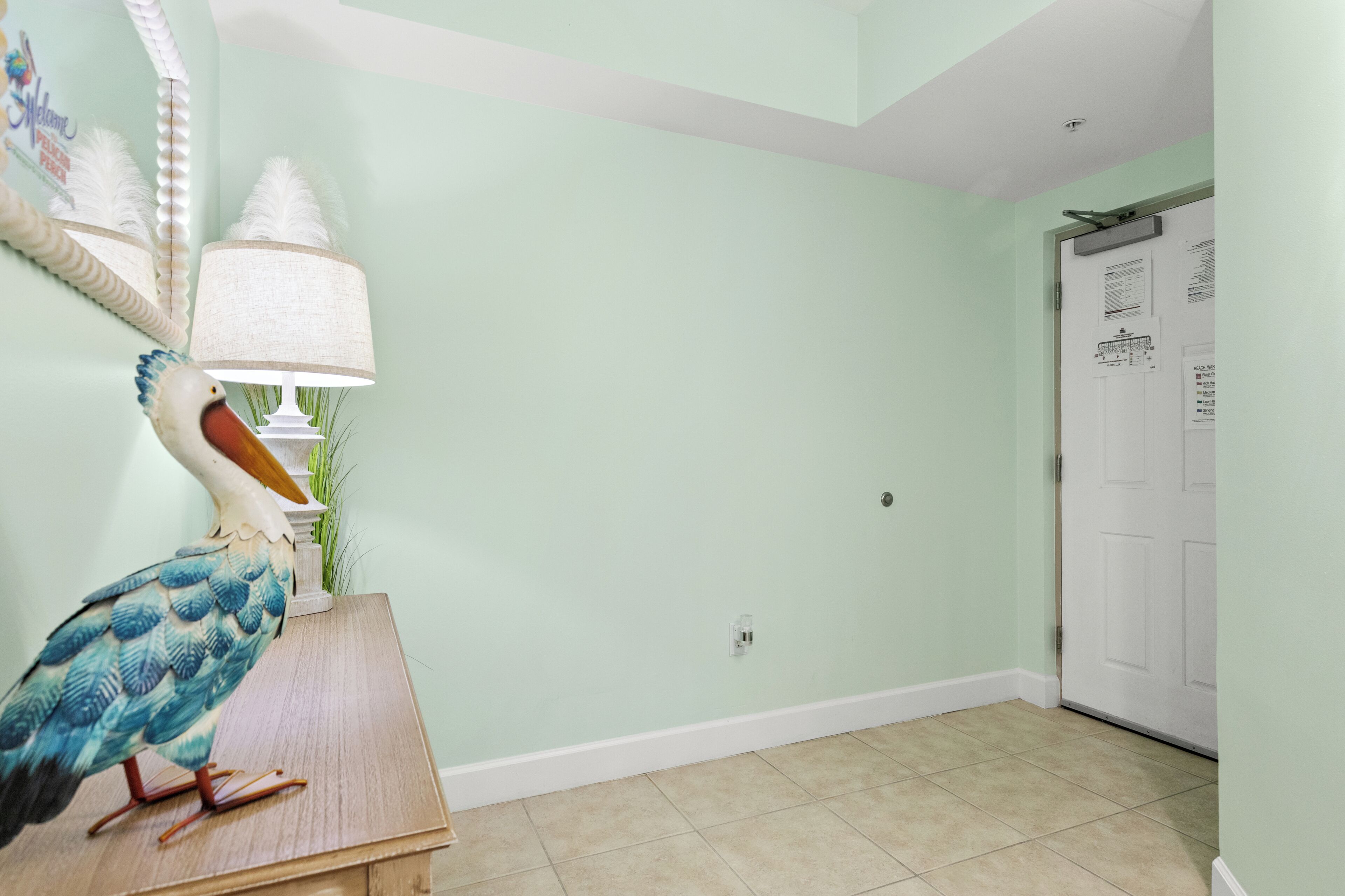 A room with a wooden table, a decorative bird sculpture, a lamp, and a door with a bulletin board.