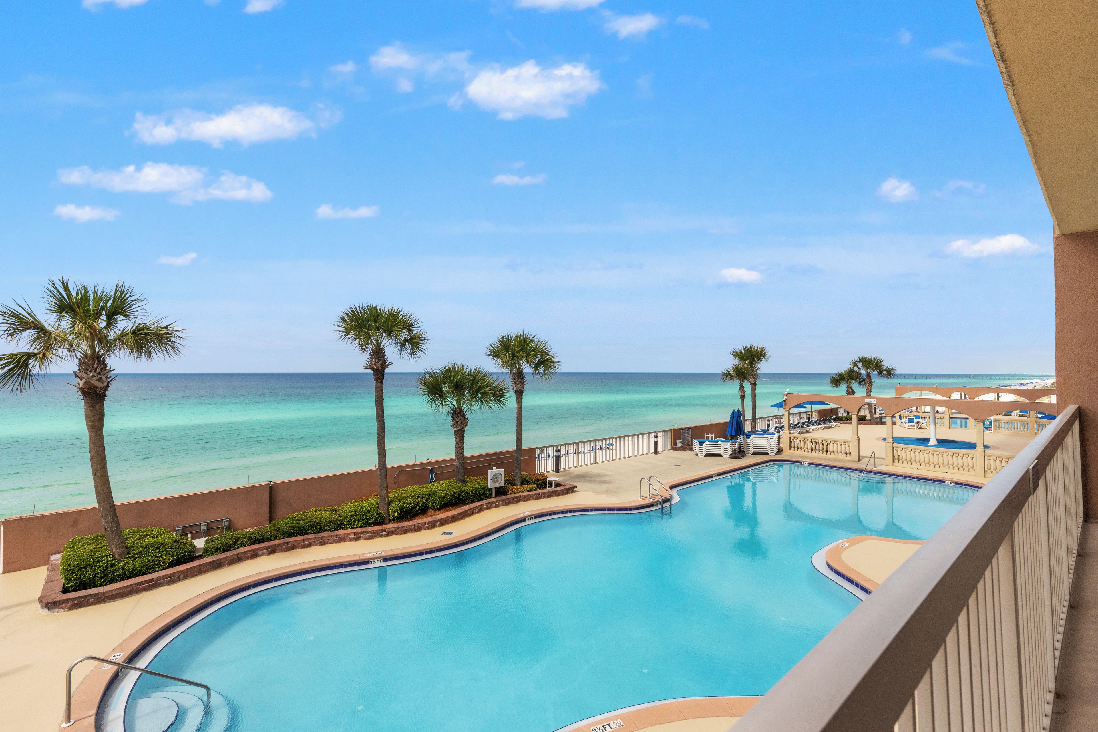 A pool with a view of the ocean, palm trees, and a beach area.