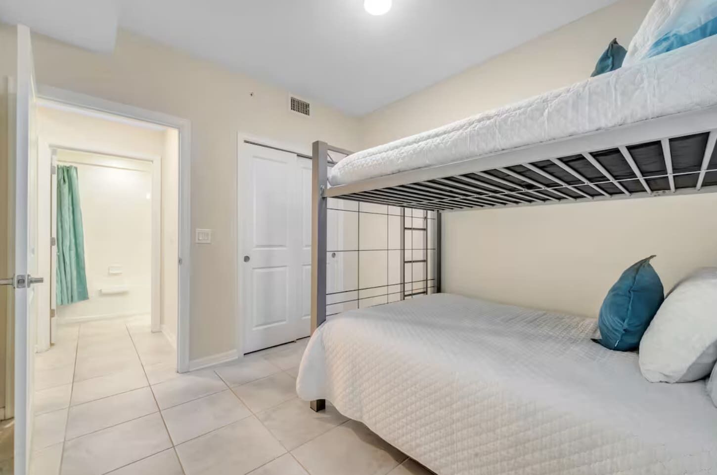 A bedroom with a bunk bed, a door leading to a bathroom, and a tiled floor.