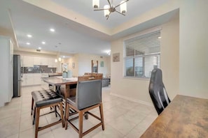 A modern kitchen with white cabinets, a dining area with a wooden table and chairs, and a large window with blinds. - Storey Lake Resort Condo w Patio5 Miles to Disney (Kissimmee)