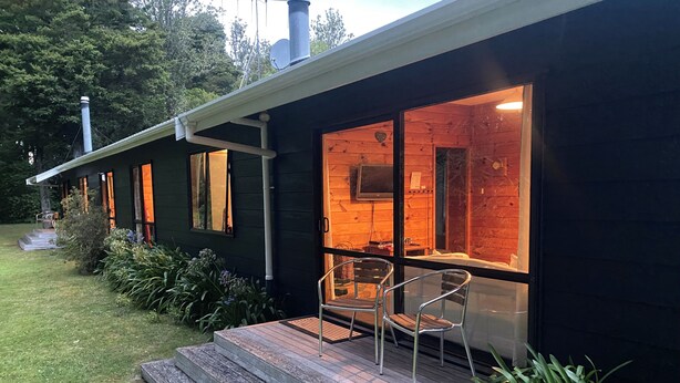 A modern house with a wooden exterior, a glass door entrance, and a small porch with two chairs. - Puka Lodge (Front dwelling) 2 mins walk to beautiful Pukawa Bay Beach Lake Taupo (Pukawa)
