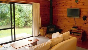 A cozy room with a sofa, a television, a fireplace, and a large window with curtains. - Puka Lodge (Front dwelling) 2 mins walk to beautiful Pukawa Bay Beach Lake Taupo (Pukawa)