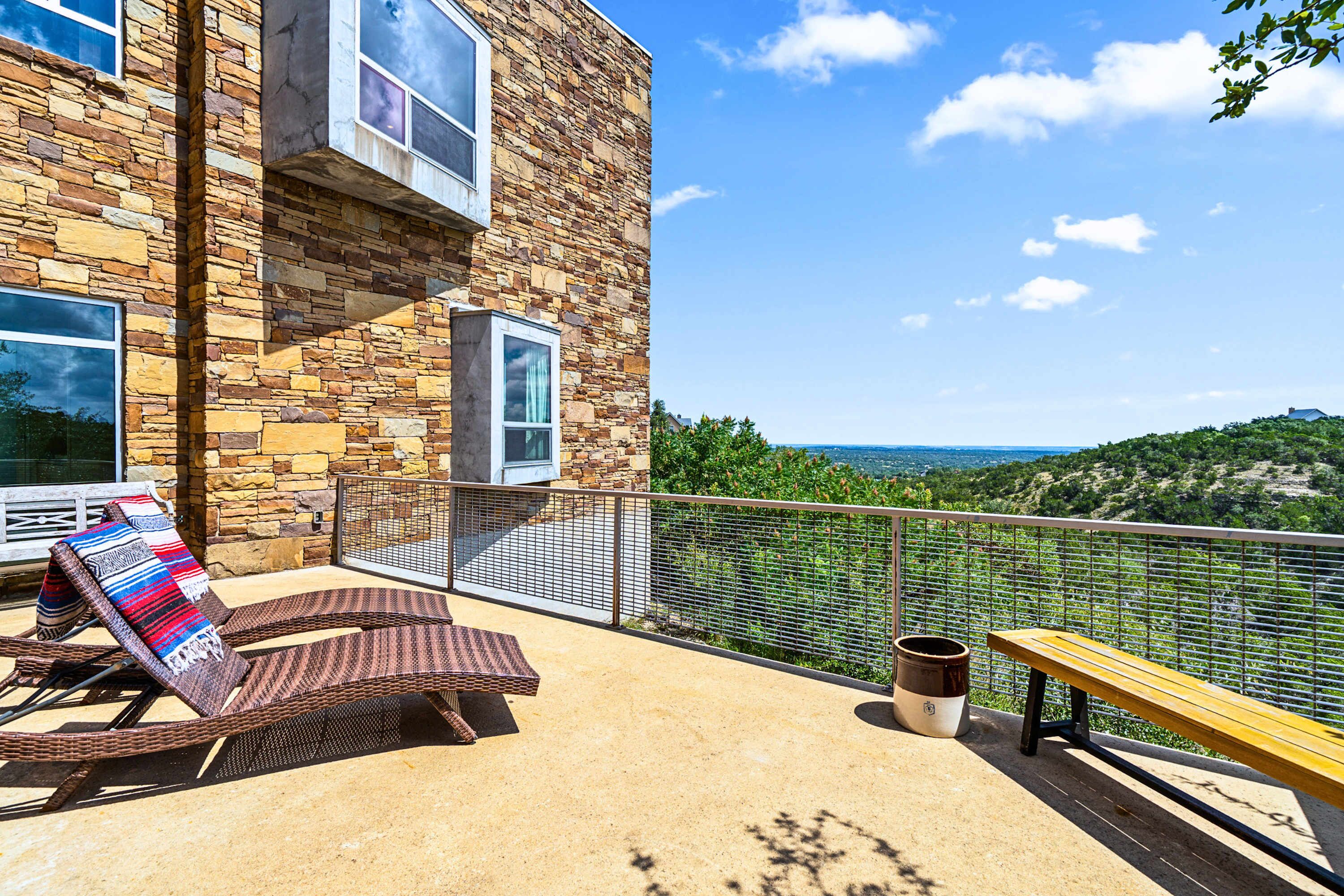 A balcony with wicker chairs and a bench, overlooking a scenic view.