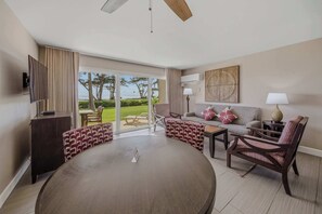 A room with a round table, sofas, a TV, and a view of the outdoors. - Oceanfront Escape | Pono Kai Resort | A103 (Kapaʻa)