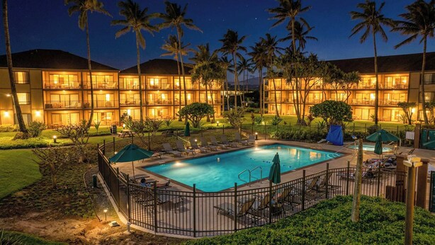 Ein Hotel mit Schwimmbad, Palmen und einem gut beleuchteten Außenbereich.