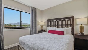 Ein Hotelzimmer mit einem großen Bett, zwei Nachttischen, einem Fenster mit Ausblick und einem Kopfteil mit geometrischem Muster.