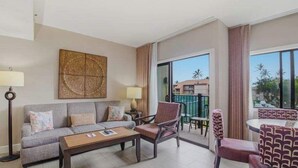 Ein Hotelzimmer mit Sofa, Sessel, Couchtisch und einem Balkon mit Sitzgelegenheit.