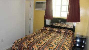 Un dormitorio con cama, ventana con cortinas, equipo de aire acondicionado y una pequeña mesa.