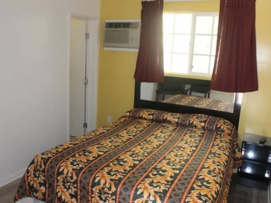 Un dormitorio con cama, ventana con cortinas, equipo de aire acondicionado y una pequeña mesa.