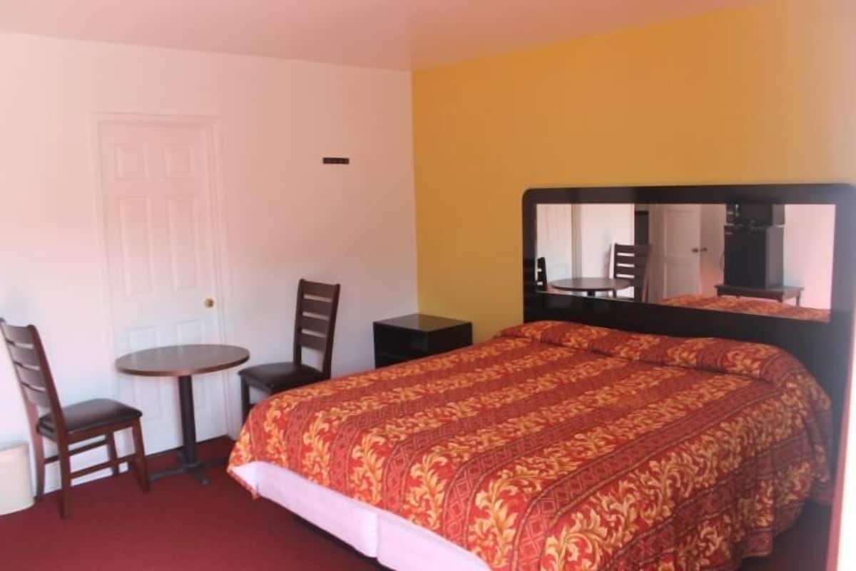 A hotel room with a bed, a desk, two chairs, a round table, and a mirror.