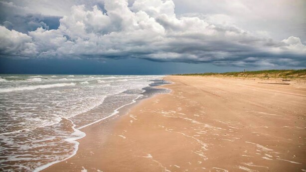 Ein Strand mit Wellen, sandigem Ufer und bewölktem Himmel.