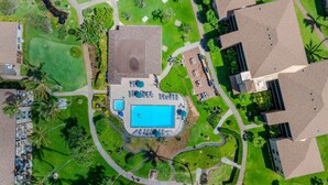 Vue aérienne d’un complexe hôtelier doté d’une piscine centrale, entourée de sentiers, de palmiers et de bâtiments modernes.