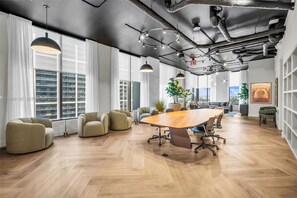 A modern conference room with a large wooden table, comfortable seating, and large windows offering city views. - 501 First Miami 1BR/1BA City Base #1208 (Miami)