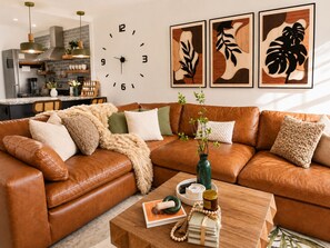 A living room with a brown leather sofa, a wooden coffee table, and a wall clock. - Romantic Riverfront Views Private Pool HotTub Fireplaces Pets BBQ Luxe Amenities (Jeffersonville)