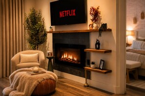 A living room with a fireplace, a sofa, a television displaying 'NETFLIX,' and a potted plant. - Romantic Waterfront Views HotTub Fireplaces BBQ Private Pool Pets Luxe Amenities (Jeffersonville)