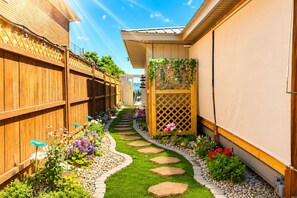 Een smal tuinpad met stapstenen, omringd door een houten hek en diverse bloeiende planten.