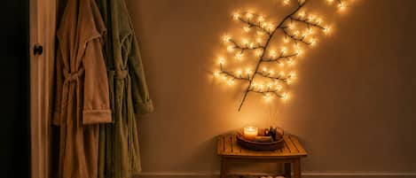 Ein Zimmer mit Holzboden, einem weißen, flauschigen Teppich, einem Holznachttisch mit Kerze und einer Wandleuchte.
