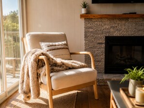 A cozy room with a cushioned chair, a fireplace, a window with a view, and a plant on a shelf. - Romantic Waterfront Views BBQ HotTub Fireplaces Private Pool Pets Luxe Amenities (Jeffersonville)